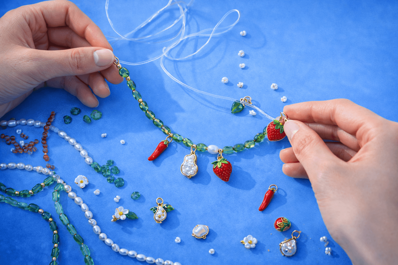 Hands threading beads onto a charm necklace
